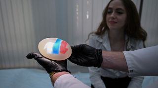 الطبيب الروسي يعرض حشوة الصدر بألوان العلم الروسي أمام إحدى زبوناته