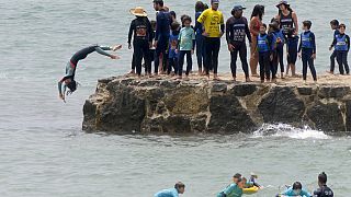 Egy fiatal szörfős ugrik a vízbe Lisszabon Carcavelos strandjánál