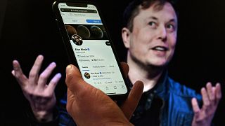 (FILES) In this file photo illustration, a phone screen displays the Twitter account of Elon Musk with a photo of him shown in the background, on April 14, 2022, in Washington