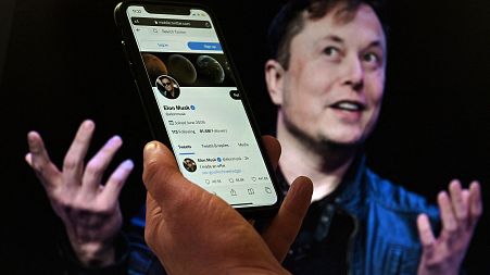 (FILES) In this file photo illustration, a phone screen displays the Twitter account of Elon Musk with a photo of him shown in the background, on April 14, 2022, in Washington
