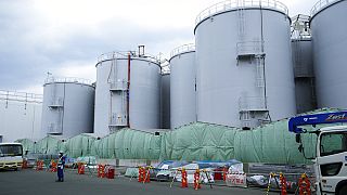 Egy helyreállítást végző alkalmazott áll a radioaktív vizet tároló tartályok előtt Okuma városában