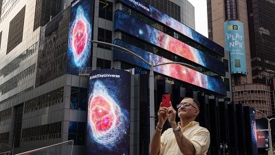 Un passant photographie les images du télescope James-Webb à Times Square, New York, le 12 juillet 2022, USA