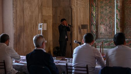 A Turkish muezzin performs the call to prayer in front of a jury, inside the Old mosque in Edirne