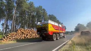 Un camión de bomeros pasa al lado de una pila de troncos de pinos en Landiras, Gironda, Francia, 19/7/2022