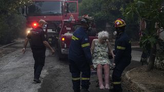 Les pompiers évacuent une femme âgée de sa maison à Penteli, en Grèce, le mardi 19 juillet 2022.