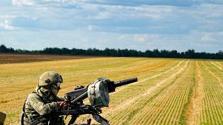 Российский солдат охраняет территорию, пока иностранные журналисты наблюдают, как фермеры собирают урожай под Мелитополем.