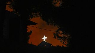 Das weiße Kreuz einer Kirche in Penteli, nordöstlich von Athen, vor einem Flammenmeer, 19.07.2022