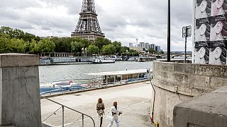 امرأتان تمشيان بجوار نهر السين أمام برج إيفيل في باريس، فرنسا، الجمعة 6 أغسطس 2021.