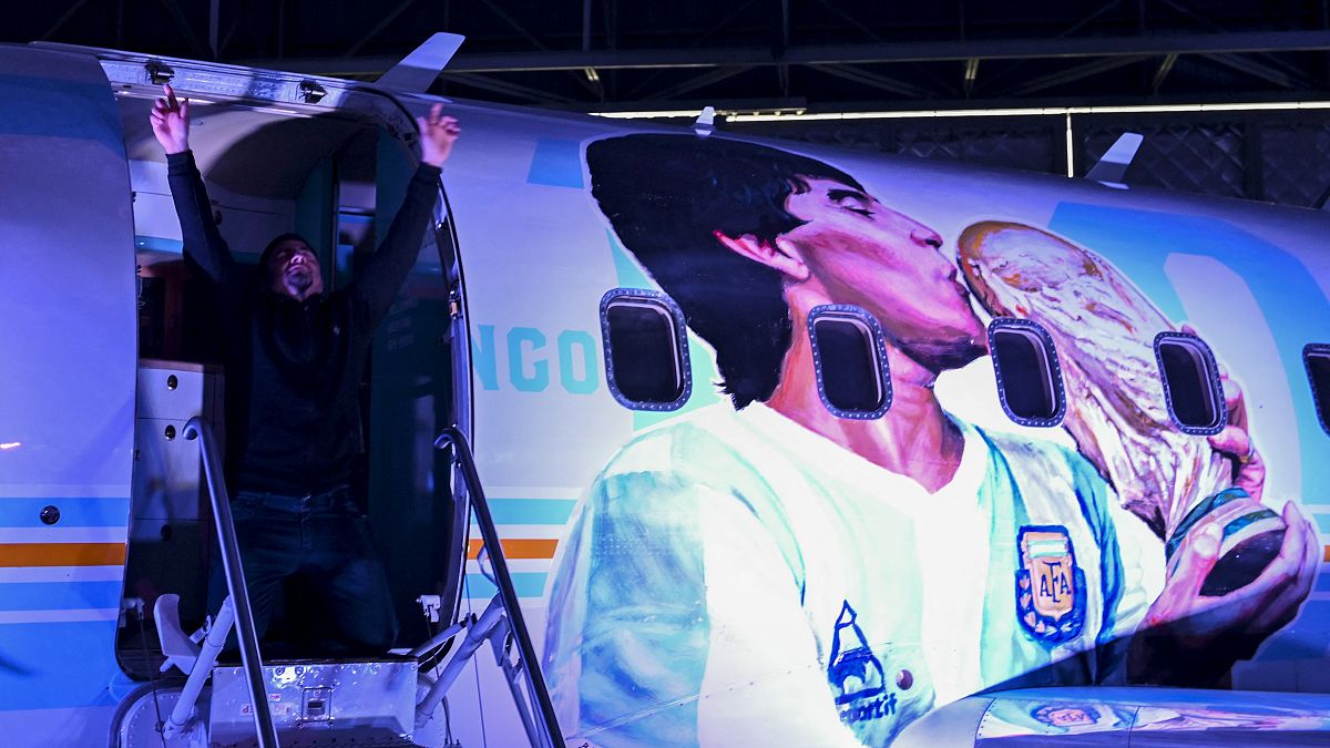  رجل يقف لالتقاط صورة في الطائرة المسماة "Tango D10S" المرسومة بصور نجم كرة القدم الراحل مارادونا، مطار مورون، مقاطعة بوينس آيرس، الأرجنتين، 23 تموز 2022