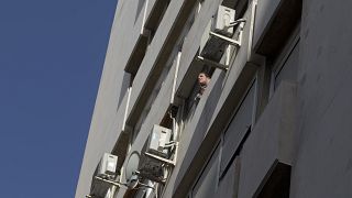 A man looks out of a window in a housing block with air conditioning units on the outside in Madrid, Spain, Tuesday, Sept. 6, 2016.