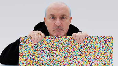 Damien Hirst poses with two of his dot paintings