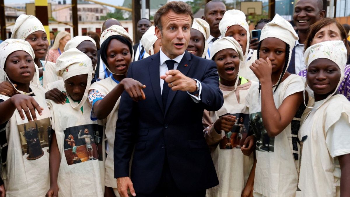 Macron poses with young women in traditional costumes as they celebrate the Abomey Treasures, during his visit to the French College in Benin, 27 July 2022. 