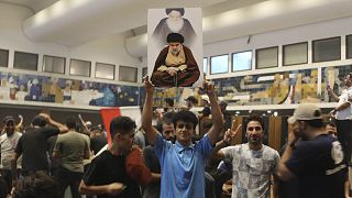 A Iraqi protester holds a poster of Shiite cleric Muqtada al-Sadr as others breach Baghdad's parliament on 27 July 2022