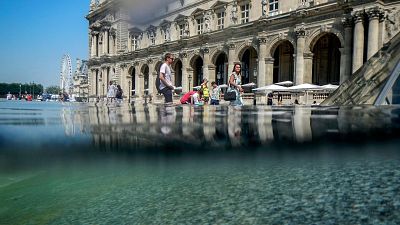 People cool off next to the fountains at Louvre Museum in Paris, France