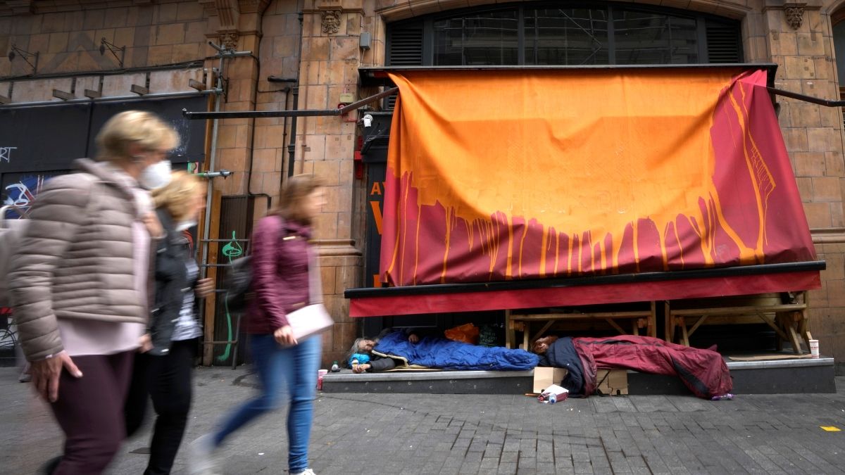 Pedestrians pass homeless people sleeping in front of a closed retail unit in London, 13 April 2022 (AP Photo/Kirsty Wigglesworth)