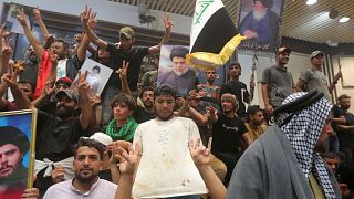 Iraqi protesters pose with national flags, a blood-stained shirt, and pictures of Shiite cleric Muqtada al-Sadr inside the Parliament building in Baghdad, 30 July 2022