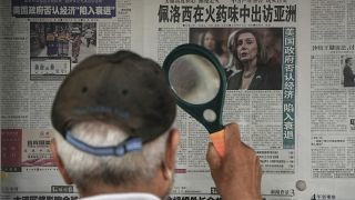 Pekingi férfi nagyítóval olvassa a hírt Pelosi ázsiai útjáról