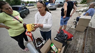 Люди осматривают содержимое коробок, которые они получили во время раздачи еды в Харькове 30 июля 2022 г.