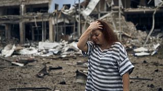 Eine Frau vor zerstörten Gebäuden nach russischem Bombardement auf Mykolajiw, Ukraine
