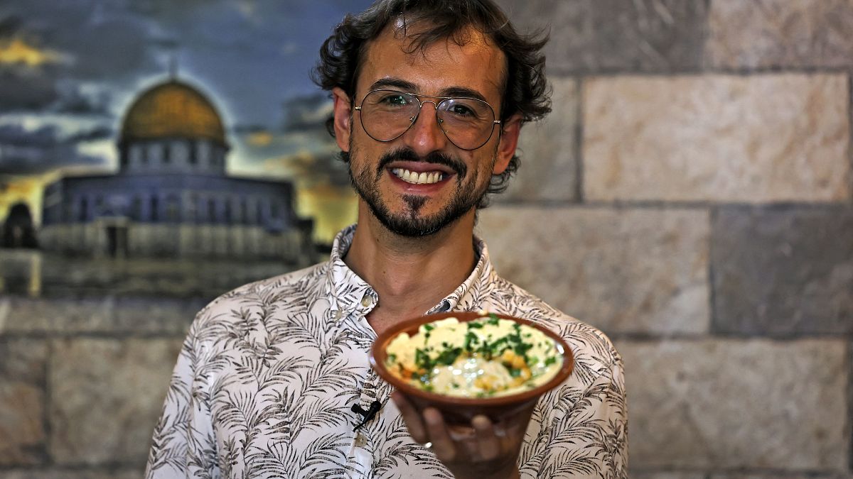 المرشد السياحي عز الدين بخاري يحمل طبق مأكولات داخل مطعم خلال جولة في البلدة القديمة في القدس. 2022/07/26