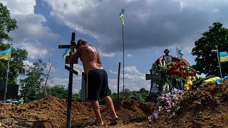 A cemetery worker places a cross on the grave of Serhiy Marchenko following his burial in Pokrovsk, Donetsk region, eastern Ukraine, Thursday, Aug. 4, 2022