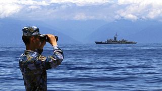 Kínai katona figyel távcsövön keresztül egy tajvani fregattot 2022. aug. 5-én.
