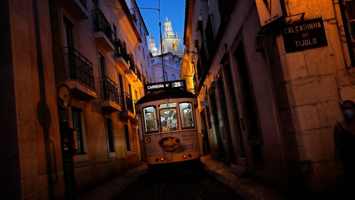 The number 28 tram, a favorite with tourists, drives through a narrow street in Lisbon's old Alfama neighborhood as night falls, Wednesday, Oct. 6, 2021. 