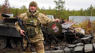 جندي أوكراني يحمل شعاراً لقوات النخبة الروسية أمام دبابة مدمرة 