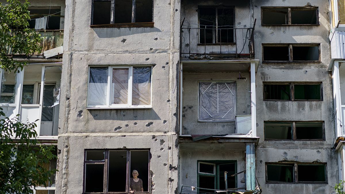 Пожилая женщина выглядывает из окна своей квартиры в Славянске после ночного обстрела (7 августа 2022 г.)