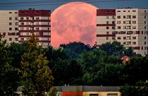 The full moon sets behind apartment houses in the outskirts of Frankfurt, Germany. August 12, 2022