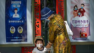 Egy nő és egy kisfiú Pekingben, maszkviselésre felszólító plakátok előtt - KÉPÜNK ILLUSZTRÁCIÓ