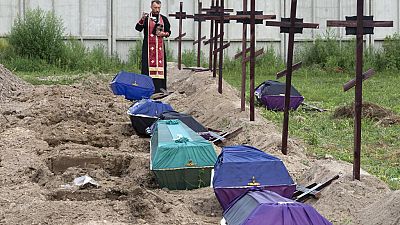 A priest prays for unidentified civilians allegedly killed by Russian troops during their occupation in Bucha, on the outskirts of Kyiv, Ukraine, Thursday, 11 Aug., 2022.