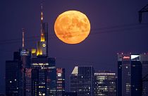 The full moon rises behind the buildings of the banking district in Frankfurt, Germany, Thursday, August 11, 2022.