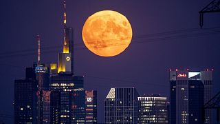 The full moon rises behind the buildings of the banking district in Frankfurt, Germany, Thursday, August 11, 2022. 