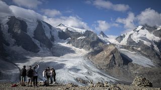 Emberek állnak a Bernina hegycsoport előtt, háttérben a Morteratsch és Pers gleccserekkel Svájcban, 2022. augusztus 10-én