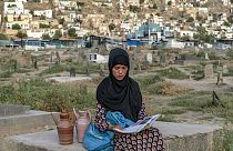 سارا، ۱۴ ساله، کتاب به دست در قبرستان کابل آب می‌فروشد، تابستان ۲۰۲۲ میلادی