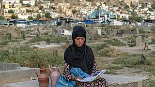 سارا، ۱۴ ساله، کتاب به دست در قبرستان کابل آب می‌فروشد، تابستان ۲۰۲۲ میلادی