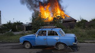 A Ukrainien man drives past a burning house hit by a shell in the outskirts of Bakhmut, Eastern Ukraine, on July 27, 2022.