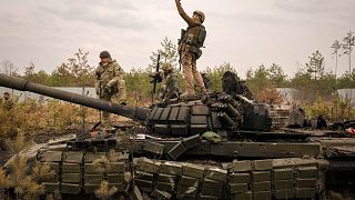 دبابة روسية مدمرة بالقرب من كييف وعليها جنديان أوكرانيان