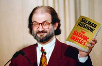 سلمان رشدی کتاب آیات شیطانی را نشان می‌دهد