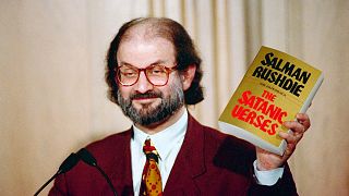 سلمان رشدی کتاب آیات شیطانی را نشان می‌دهد