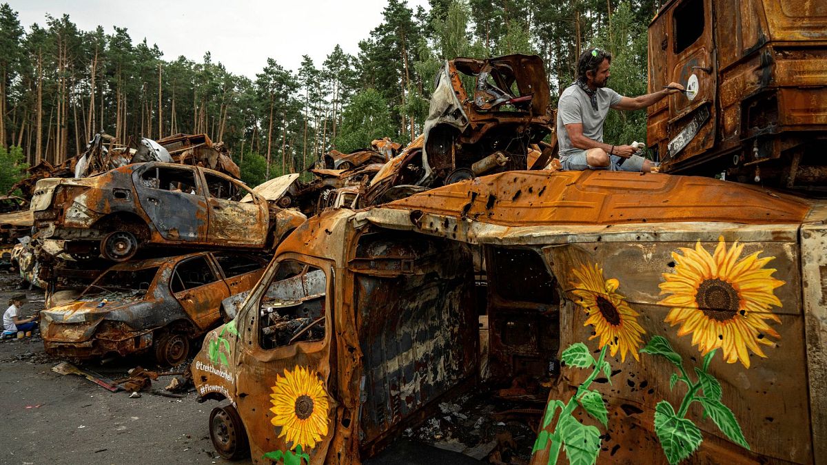 American artist Trek Thunder Kelly paints sunflowers on cars which were destroyed by Russian attack in Irpin