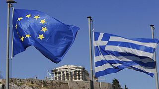 The Greek, right, and the European flags wave under the ancient Acropolis hill in Athens