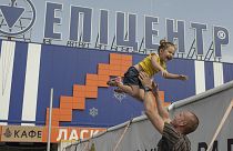 An escapee from the vicinity of the Zaporizhzhia nuclear power plant entertains his daughter below a sign that says "Epicentre", August 2022