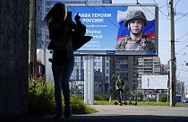 Une femme photographie un panneau publicitaire affichant le portrait d'un soldat et l'inscription "Gloire aux héros de Russie" à Saint-Pétersbourg, Russie le 20 août 2022.