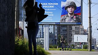 Une femme photographie un panneau publicitaire affichant le portrait d'un soldat et l'inscription "Gloire aux héros de Russie" à Saint-Pétersbourg, Russie le 20 août 2022.