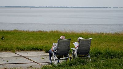 An elderly couple read as they sit on lawn chairs in front of the Schelde River in Bath, Netherlands, on Friday, July 22, 2022.