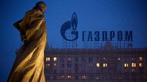 A monument to Ukrainian poet and writer Taras Shevchenko is silhouetted against a building with a sign advertising Russia's natural gas giant Gazprom, in Moscow.