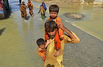 Un hombre lleva a sus dos hijos en brazos en una zona inundada de Jaffarabad, en la provincia de Baluchistán
