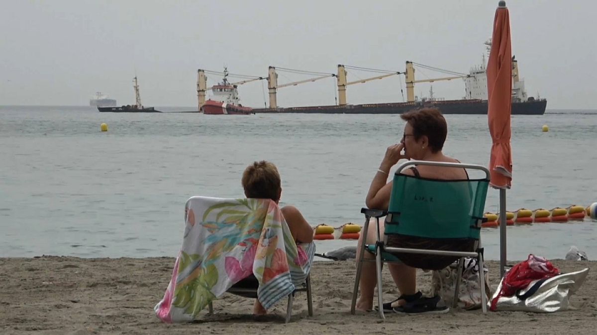 Dos mujeres observan el buque varado frente a la costa, en la Bahía de Gibraltar, tras sufrir una colisión